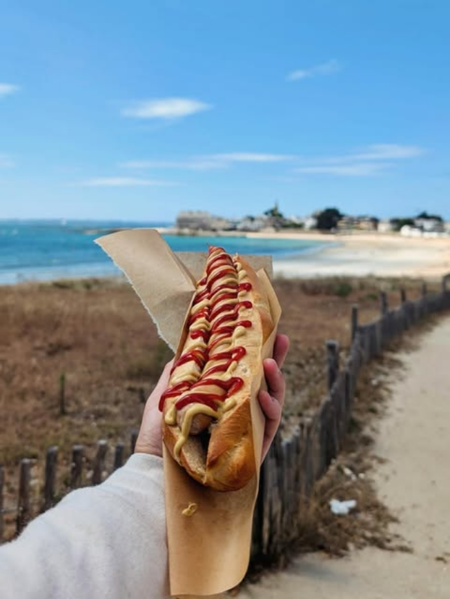Hot-dog tenu en main devant la plage de Toulhars